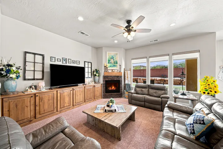 Living area featuring a stone-surround fireplace, built-in wooden cabinetry, recessed lighting, ceiling fan, and multiple windows