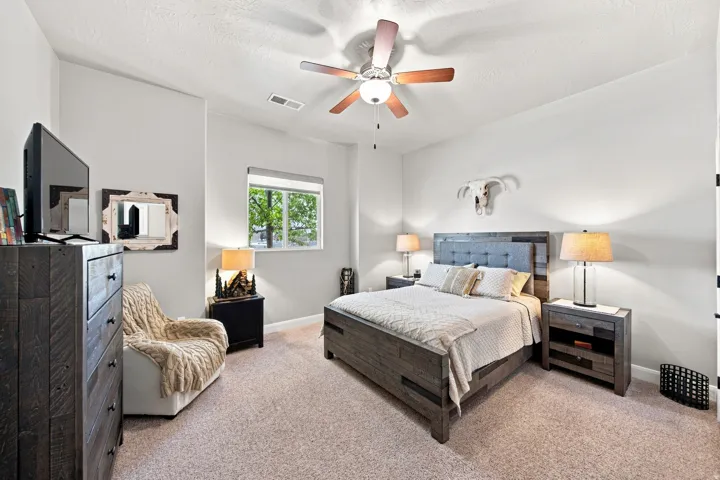 Carpeted interior room featuring a window with exterior tree scenery, a ceiling fan with integrated lighting, and light-toned wall finishes