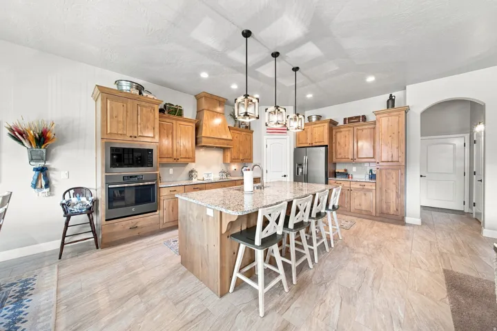 Spacious kitchen featuring natural wood cabinetry, a large kitchen island with counter seating, granite countertops, and stainless steel appliances