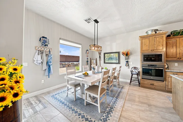 Dining area featuring a contemporary chandelier, large window, tile flooring, and integrated kitchen cabinetry with built-in appliances