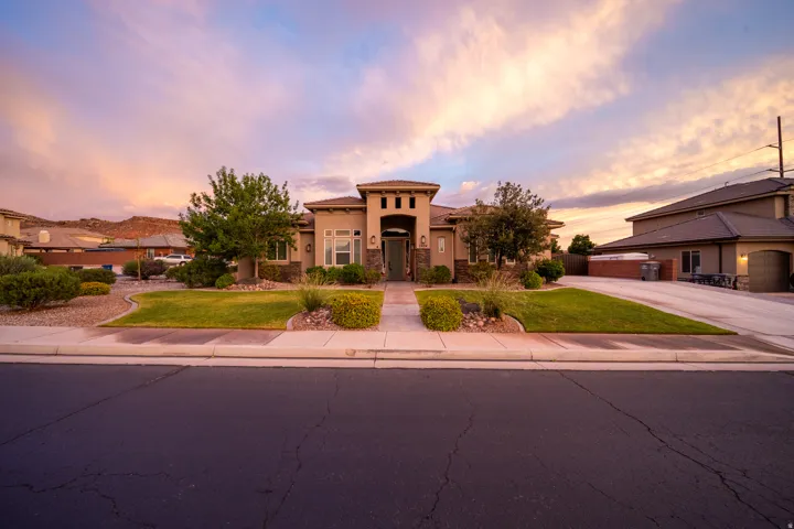 Stucco exterior with stone accents, a covered entry, established landscaping, a concrete driveway, and an attached garage