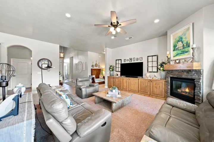 Living area featuring a stone-clad fireplace with a wood mantel, built-in cabinetry, ceiling fan, recessed lighting, and arched doorways