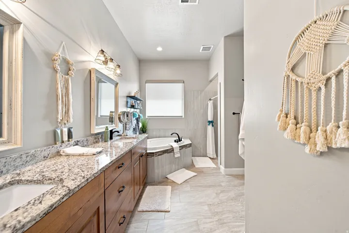 Spacious bathroom featuring a double vanity with granite countertops, wood-finish cabinetry, a built-in soaking tub, and a shower enclosure