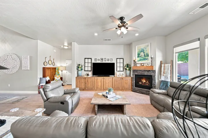 Spacious living area featuring a corner fireplace with stone surround and wood mantel, built-in cabinetry, and a ceiling fan with integrated lighting