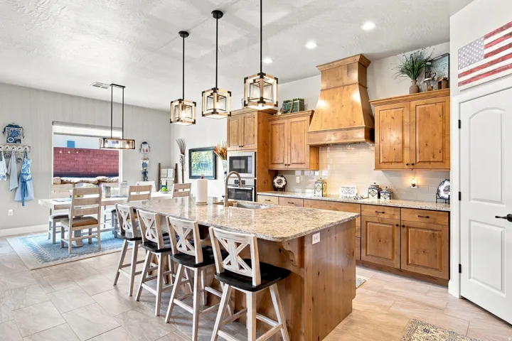 Gourmet kitchen featuring a large central island with seating, natural wood cabinetry, light-toned countertops, tile flooring, and pendant lighting