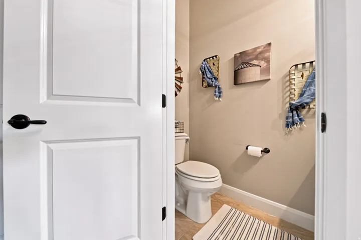 White two-panel interior door with black hardware, opening into a room with light tan walls, a white toilet, and light-toned tile flooring