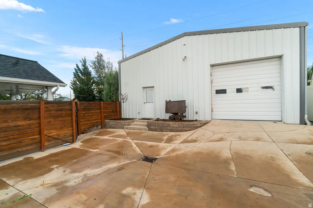 Metal utility building with a large roll-up garage door, side entry door, and concrete patio area