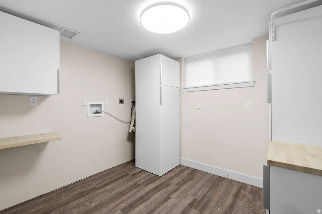 Dedicated utility space featuring wood-finish flooring, white cabinetry, a built-in shelf, and a window with a roller shade