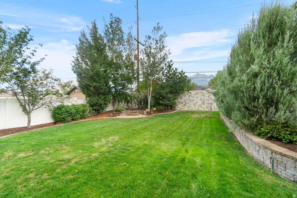 Spacious green lawn with a white privacy fence, mature trees, a stone retaining wall, and a raised planting bed