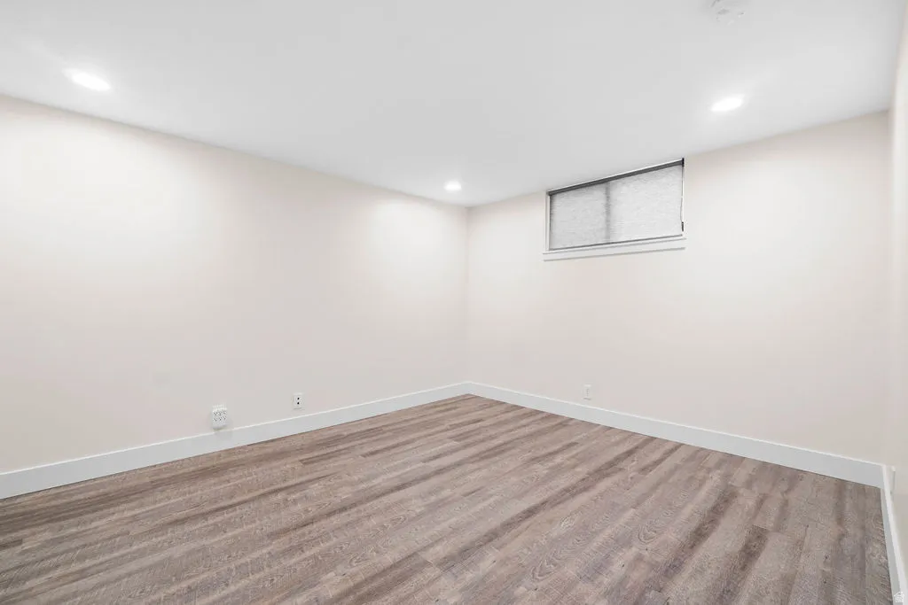 Spacious room featuring wood-finish flooring, recessed lighting, a window with privacy covering, light-toned walls, and white baseboards