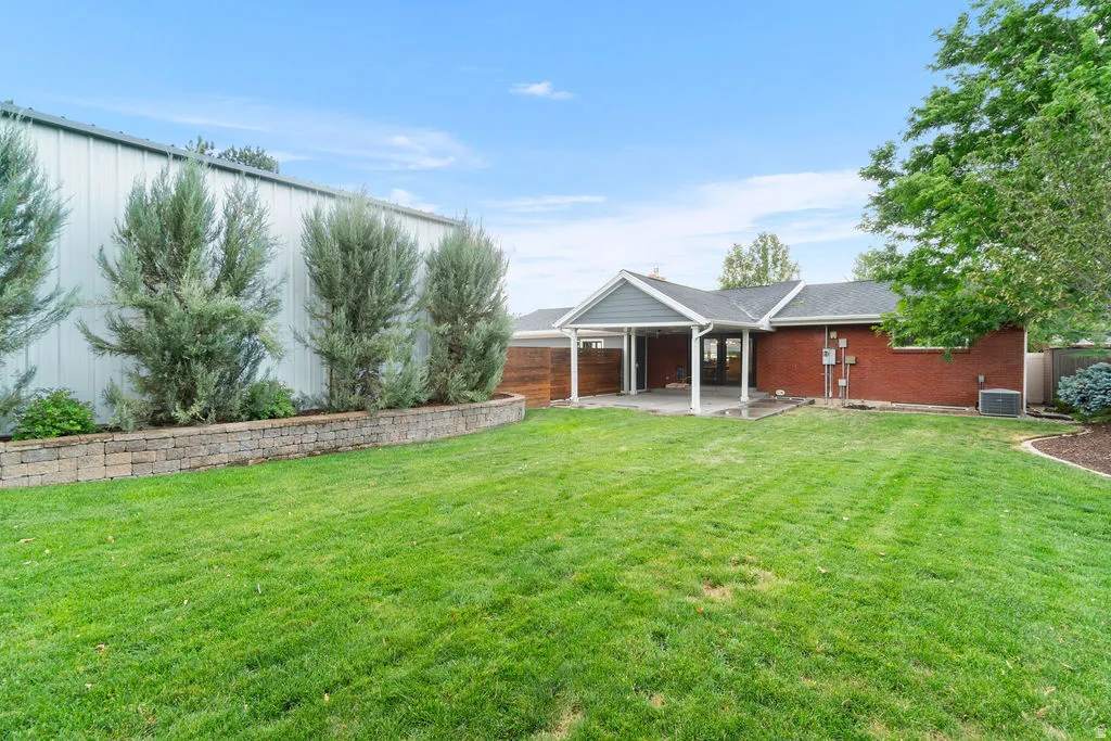 Expansive green lawn with a retaining wall, mature perimeter trees, and a covered patio