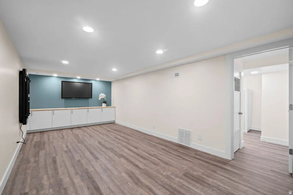 Spacious room featuring wood-finish flooring, recessed lighting, and a custom built-in media console with white cabinetry and a wood-finish countertop
