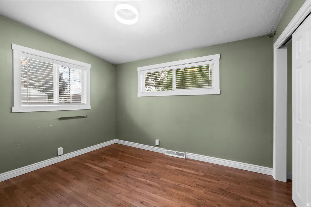 Hardwood flooring provides a warm foundation for this room featuring two windows with white trim and blinds, a white ceiling, and a flush-mount light fixture