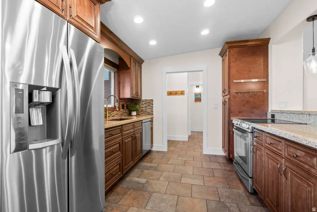 Kitchen featuring stainless steel appliances, wood cabinetry, granite countertops, and tile flooring