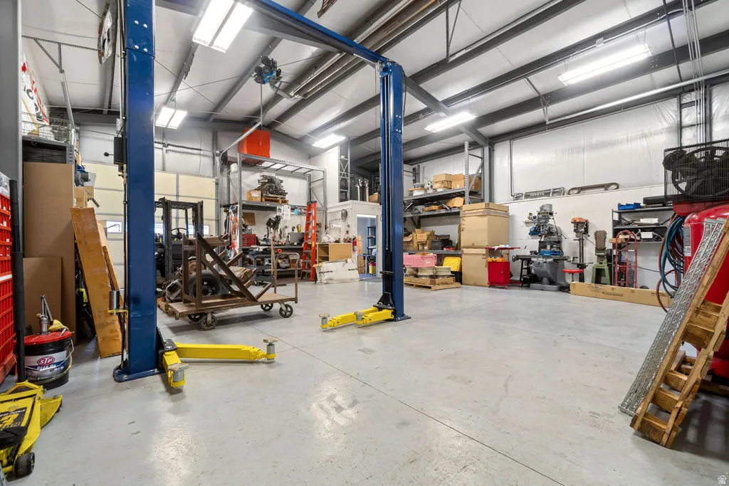 Spacious commercial garage featuring a two-post vehicle lift, polished concrete flooring, extensive overhead lighting, high ceilings with exposed steel beams, and a large roll-up door