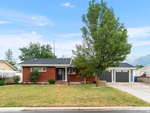 Brick exterior home with a two-car garage, expansive driveway, and a manicured front lawn
