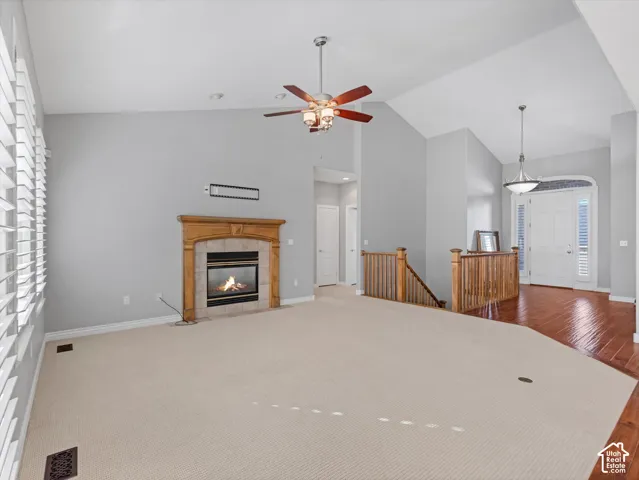 Spacious living area featuring a fireplace with a wood mantle, vaulted ceilings, and a ceiling fan