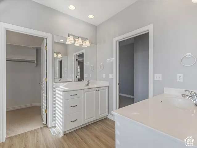 Double vanity bathroom featuring white cabinetry with brushed nickel hardware, expansive countertop space, and wood-finish flooring