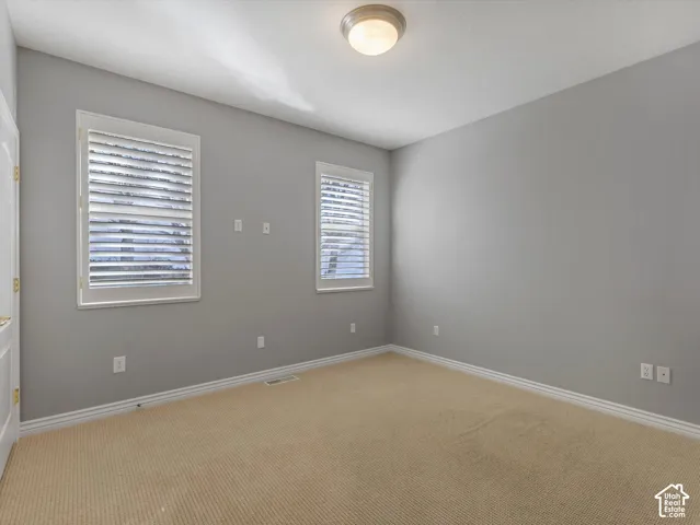 Bedroom featuring two windows with white plantation shutters, neutral gray walls, and light tan carpeting