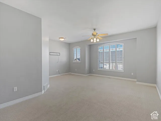 Spacious room featuring neutral carpeting, light gray walls, a ceiling fan with integrated lighting, and arched windows with plantation shutters