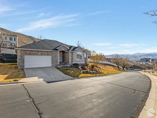 Curb appeal featuring a stone and siding exterior, an attached garage, a paved driveway, and a bay window