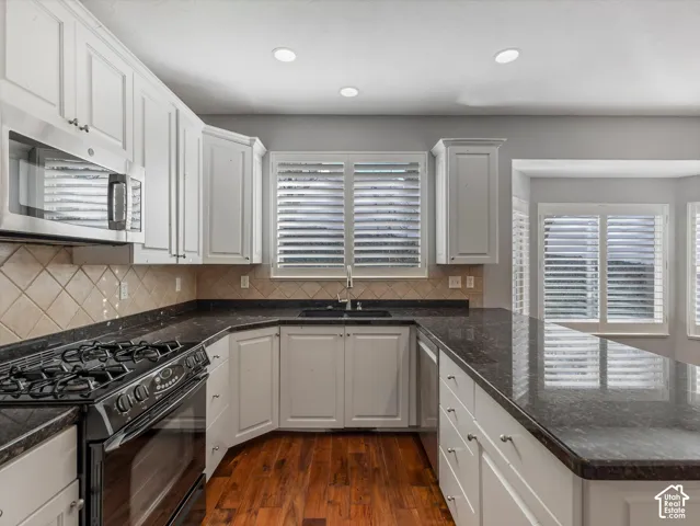 Kitchen featuring white cabinetry, dark granite countertops, stainless steel appliances, and wood-finish flooring