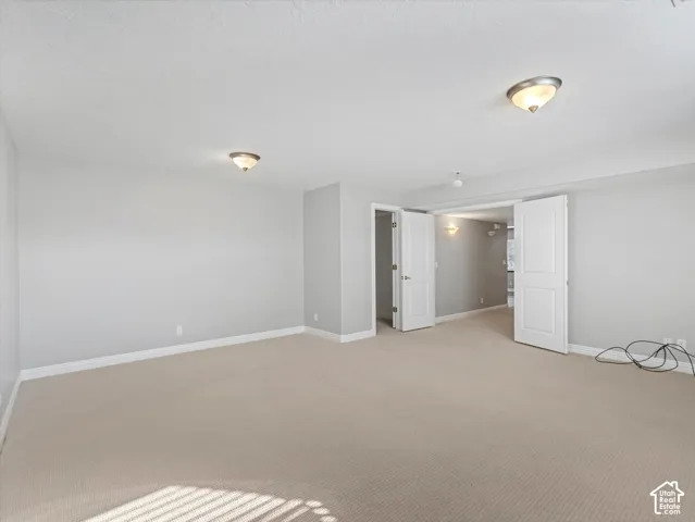 Expansive room featuring neutral-toned carpeting, light gray wall paint, and white baseboards