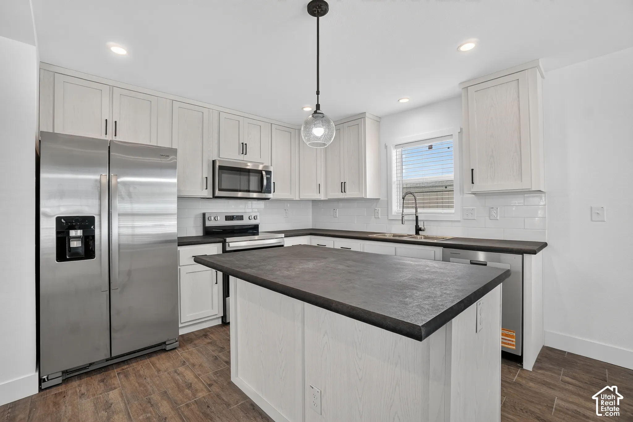 Kitchen featuring a central island with dark countertops, white shaker-style cabinetry, stainless steel appliances, and wood-finish flooring