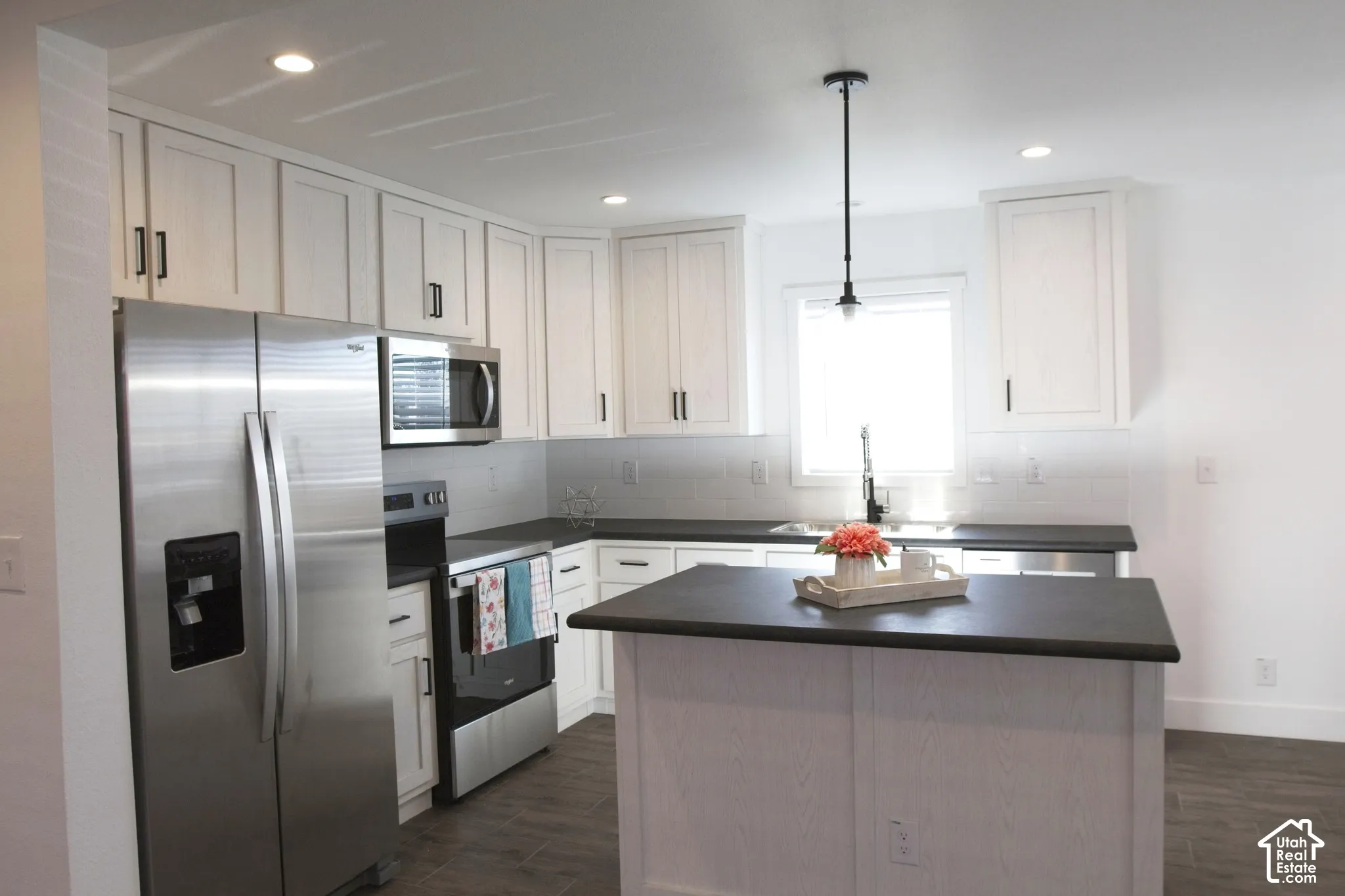 Kitchen featuring white shaker-style cabinetry, dark solid-surface countertops, wood-finish flooring, stainless steel appliances, and a center island