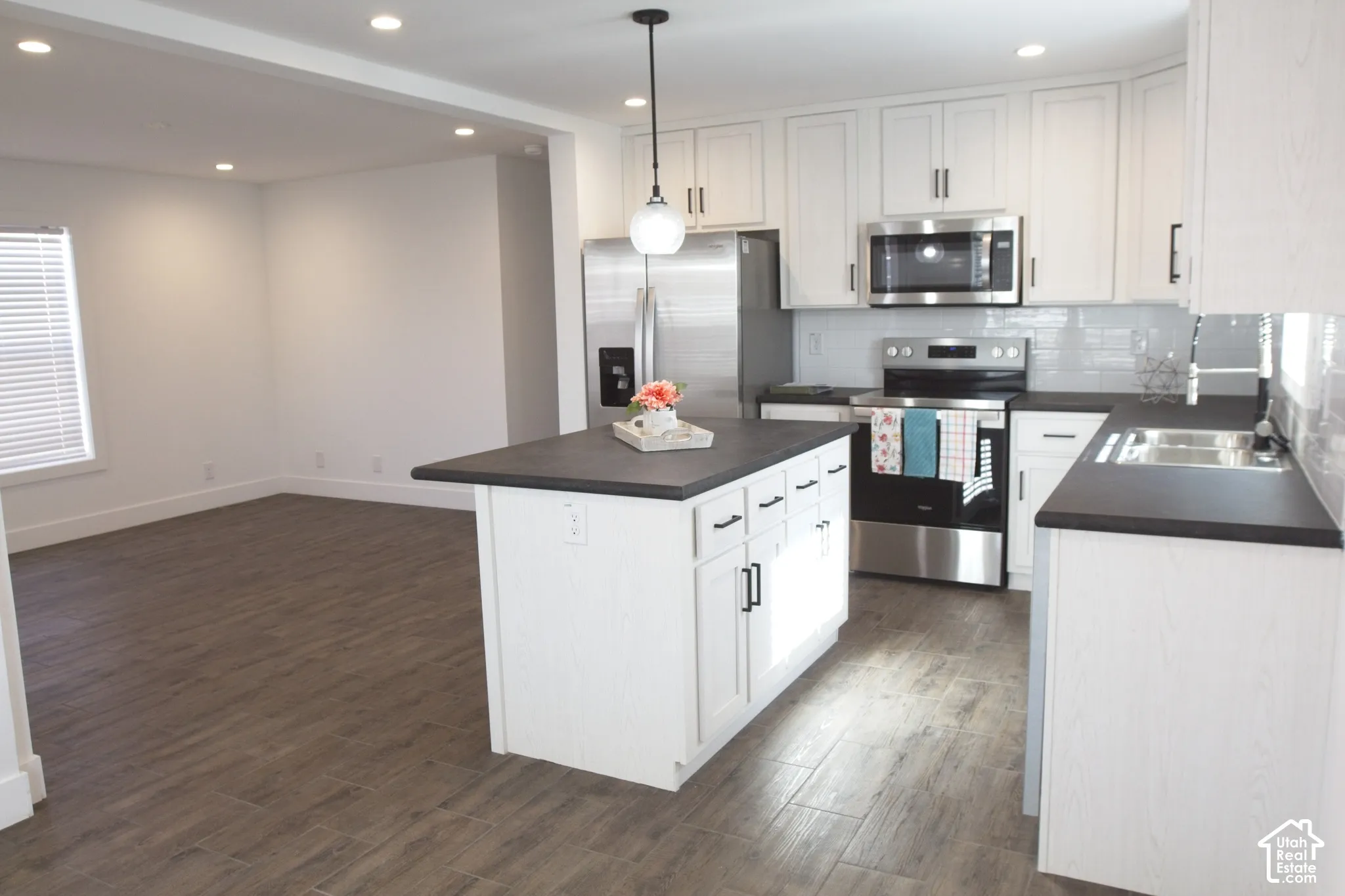 Kitchen featuring white cabinetry, matte black hardware, dark solid-surface countertops, stainless steel appliances, and wood-finish tile flooring