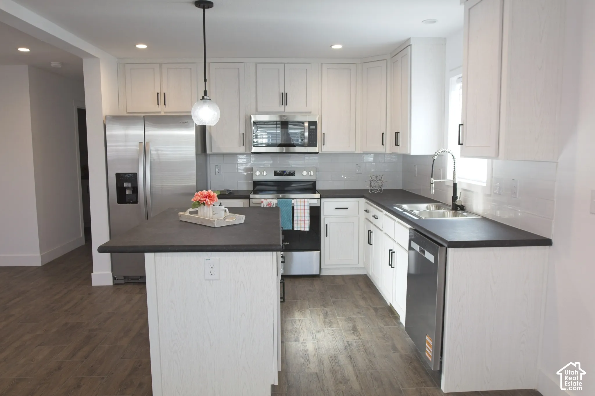 Kitchen featuring white shaker-style cabinetry, a dark matte-finish island, wood-finish flooring, stainless steel appliances, and a glass pendant light
