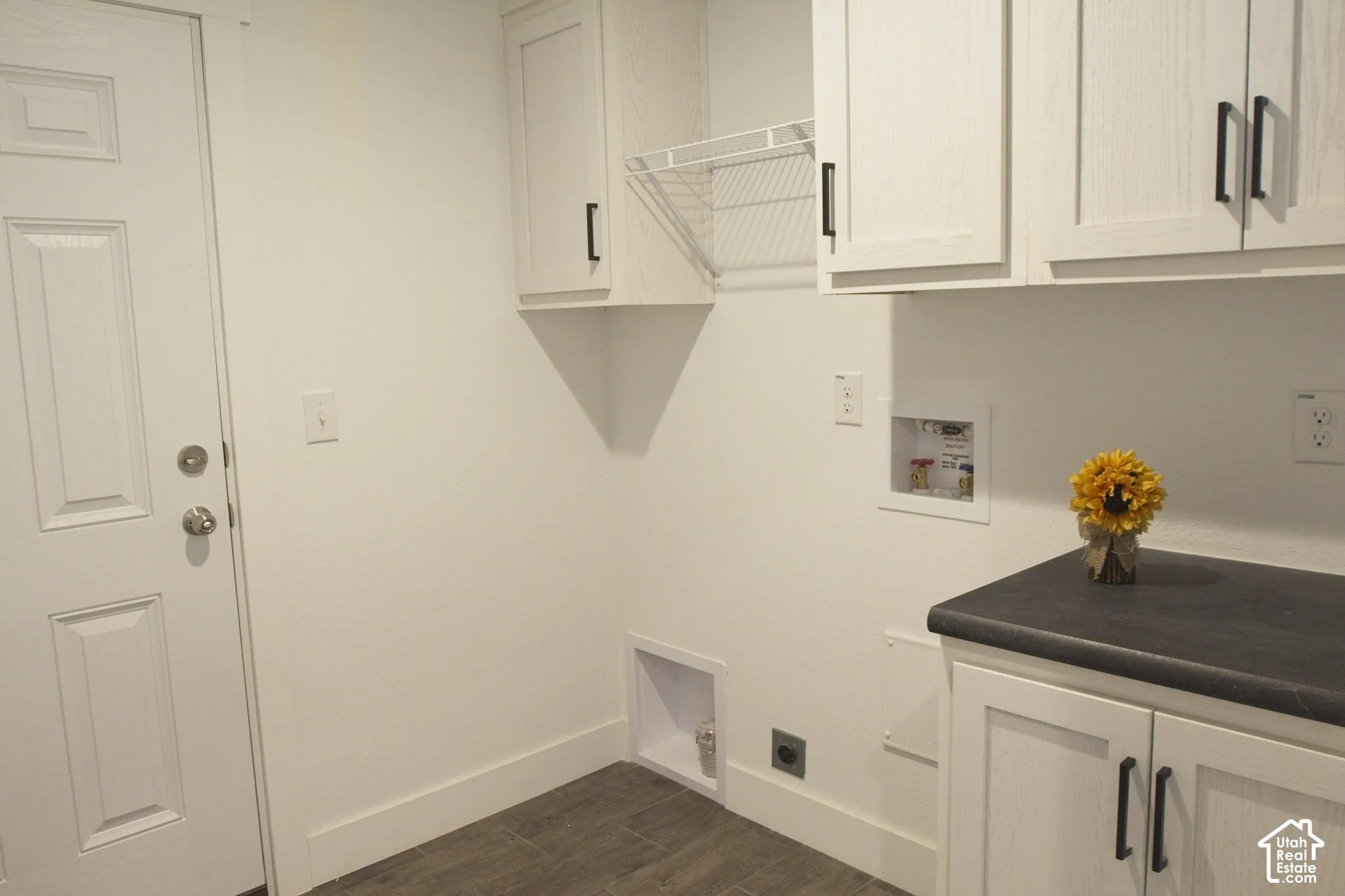 Utility room featuring white wood-grain cabinetry, matte black hardware, dark solid-surface countertop, and wood-finish flooring