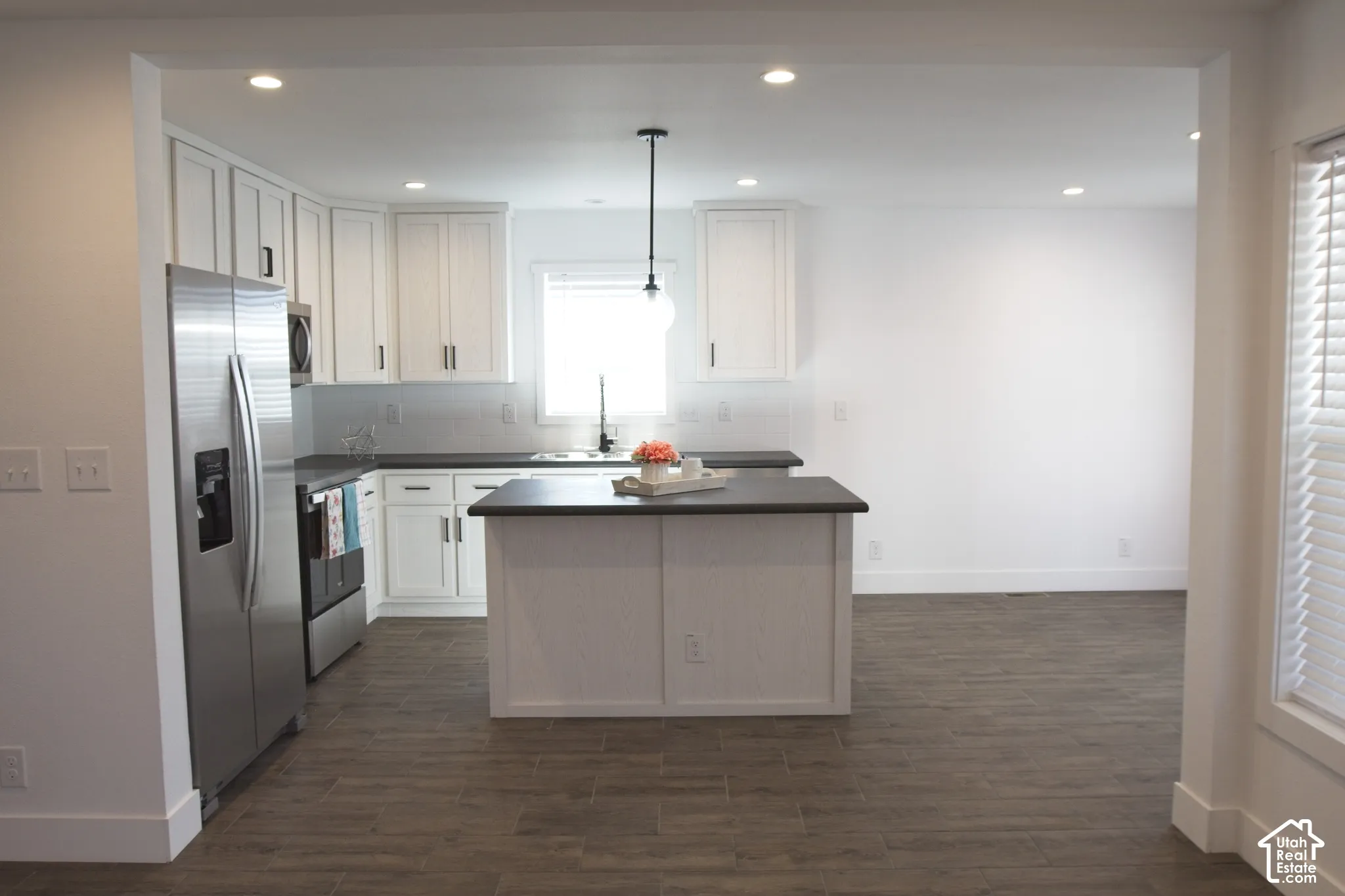 Kitchen featuring white cabinetry, center island with a dark countertop, stainless steel refrigerator, wood-finish flooring, and recessed ceiling lighting