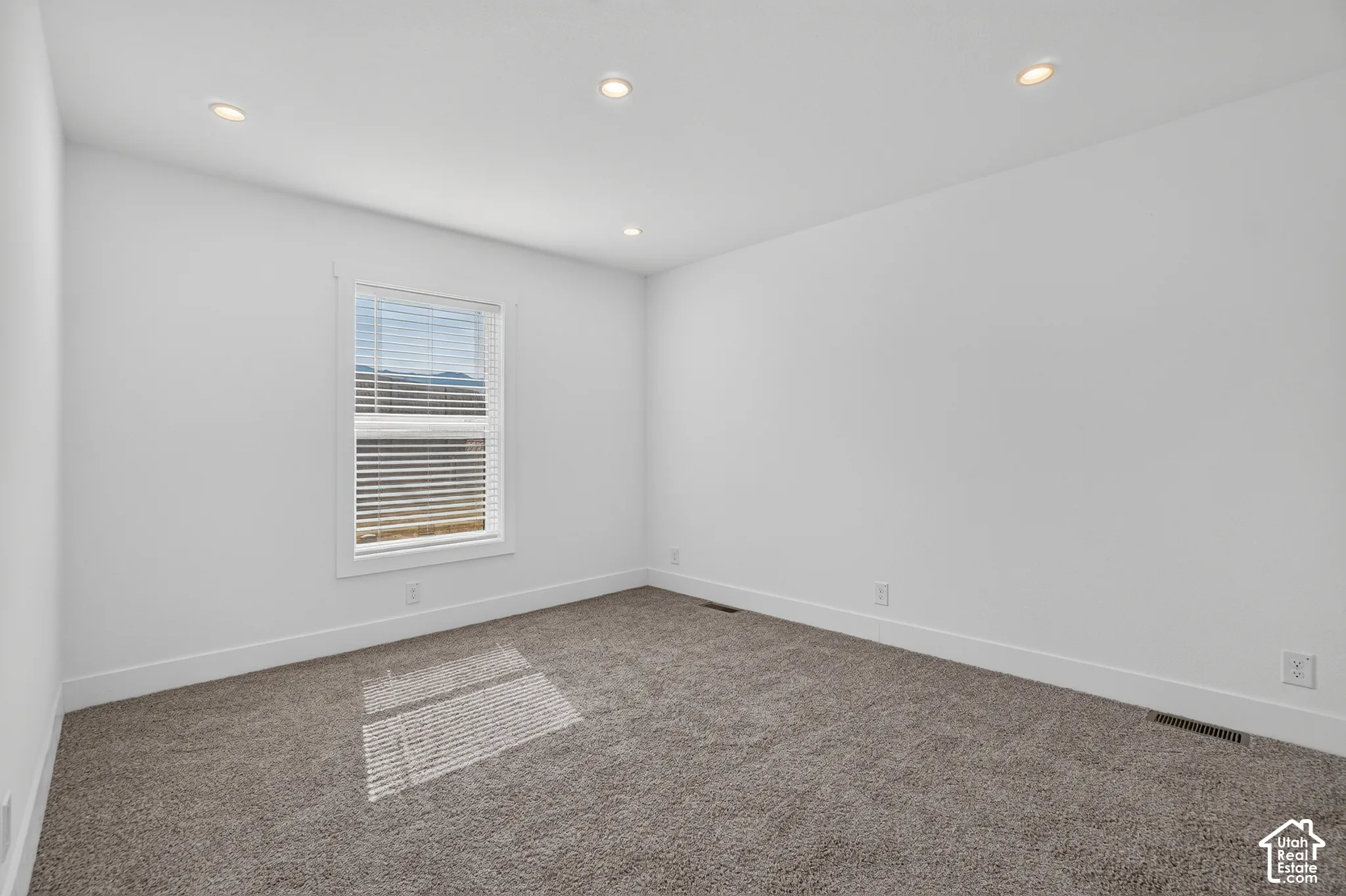 Carpeted room with white walls, recessed lighting, and a single window featuring horizontal blinds