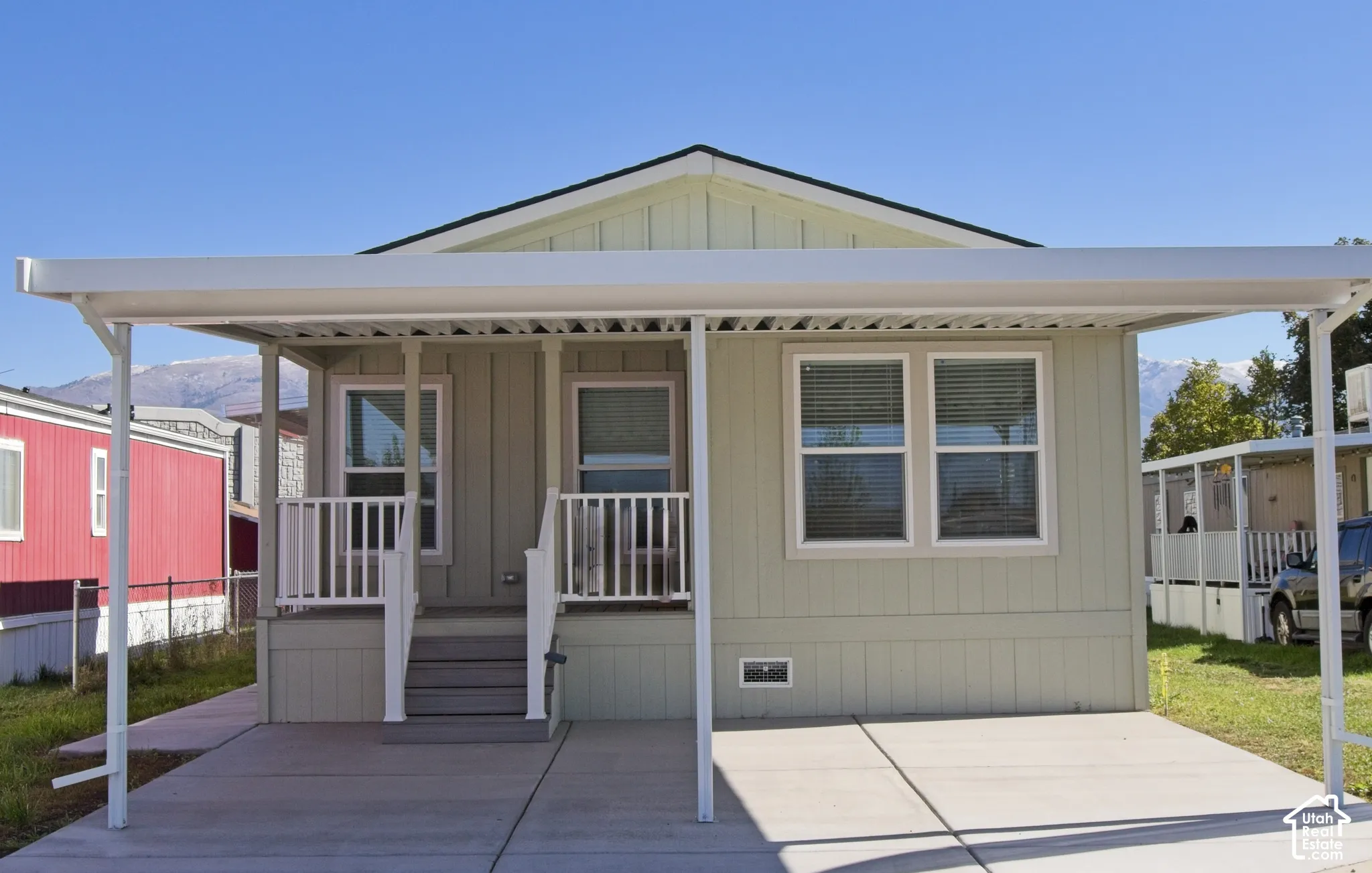 Light green exterior siding with a covered carport, raised porch, white railings, and concrete driveway