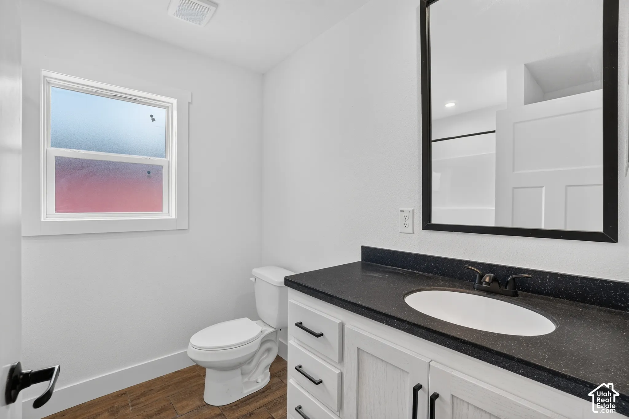 Bathroom featuring a single vanity with a dark countertop, white cabinetry with black hardware, and an oval undermount sink with a black faucet