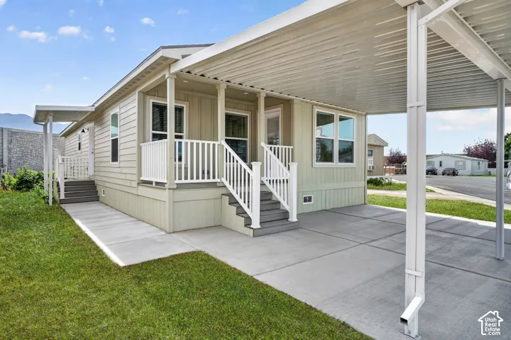 Light-colored siding exterior featuring a covered carport, front porch with white railings, multiple windows, and a concrete walkway