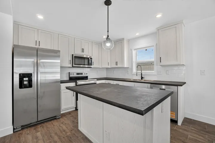 Kitchen featuring a central island with dark countertops, white shaker-style cabinetry, stainless steel appliances, and wood-finish flooring