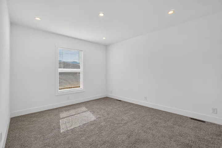 Carpeted room with white walls, recessed lighting, and a single window featuring horizontal blinds