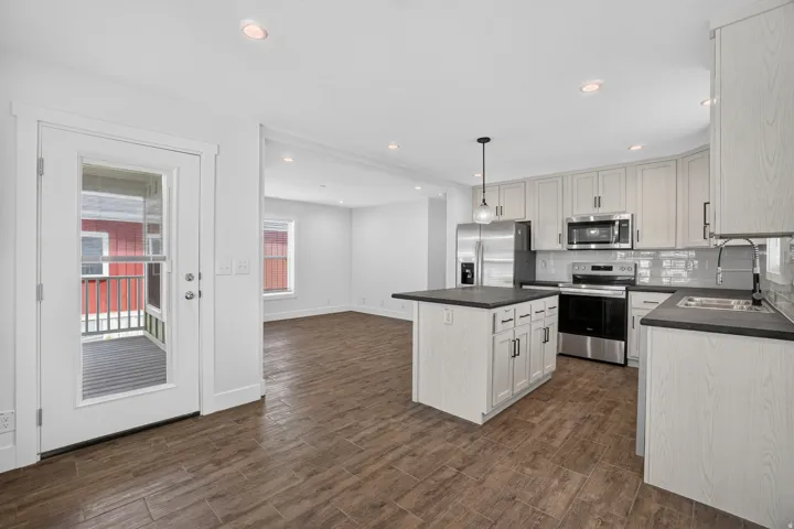 Open-concept kitchen with light wood-finish cabinetry, dark countertops, and stainless steel appliances