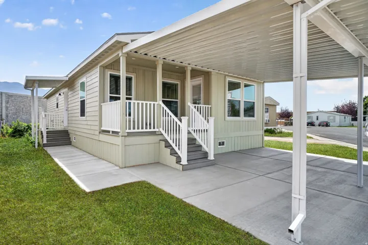 Light-colored siding exterior featuring a covered carport, front porch with white railings, multiple windows, and a concrete walkway