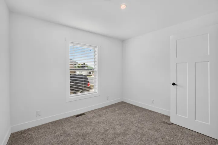 Carpeted room with a single window featuring blinds, a white paneled door with matte black hardware, recessed ceiling lighting, and crisp white trim