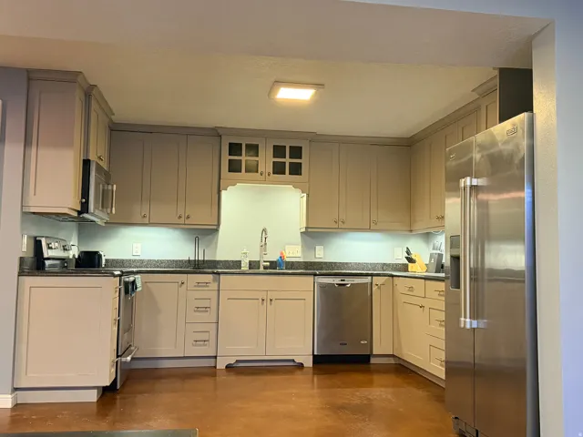 Modern kitchen featuring extensive cabinetry, stainless steel appliances, dark granite countertops, and under-cabinet lighting