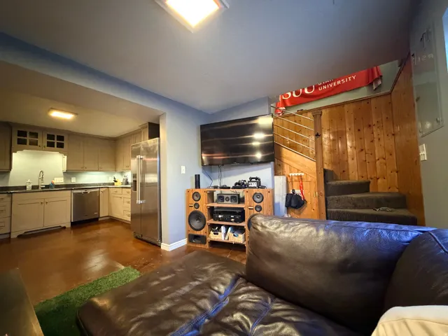 Open-concept living area featuring a kitchen with stainless steel appliances, dark countertops, and light-colored cabinetry
