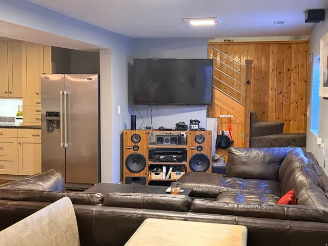 Open-concept living area featuring a kitchen with light wood-finish cabinetry, stainless steel refrigerator, and stone countertops