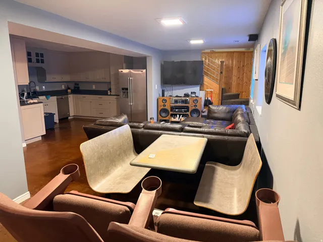 Open-concept living area featuring wood-finish flooring, a kitchen with light cabinetry, black countertops, and stainless steel appliances