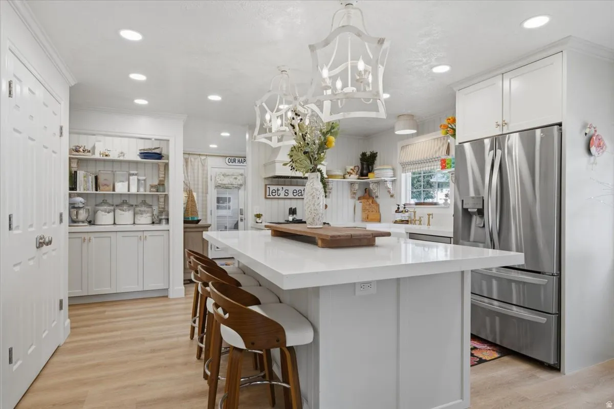 Kitchen featuring a large central island with seating, white shaker cabinetry, recessed lighting, stainless steel refrigerator, and wood-finish flooring
