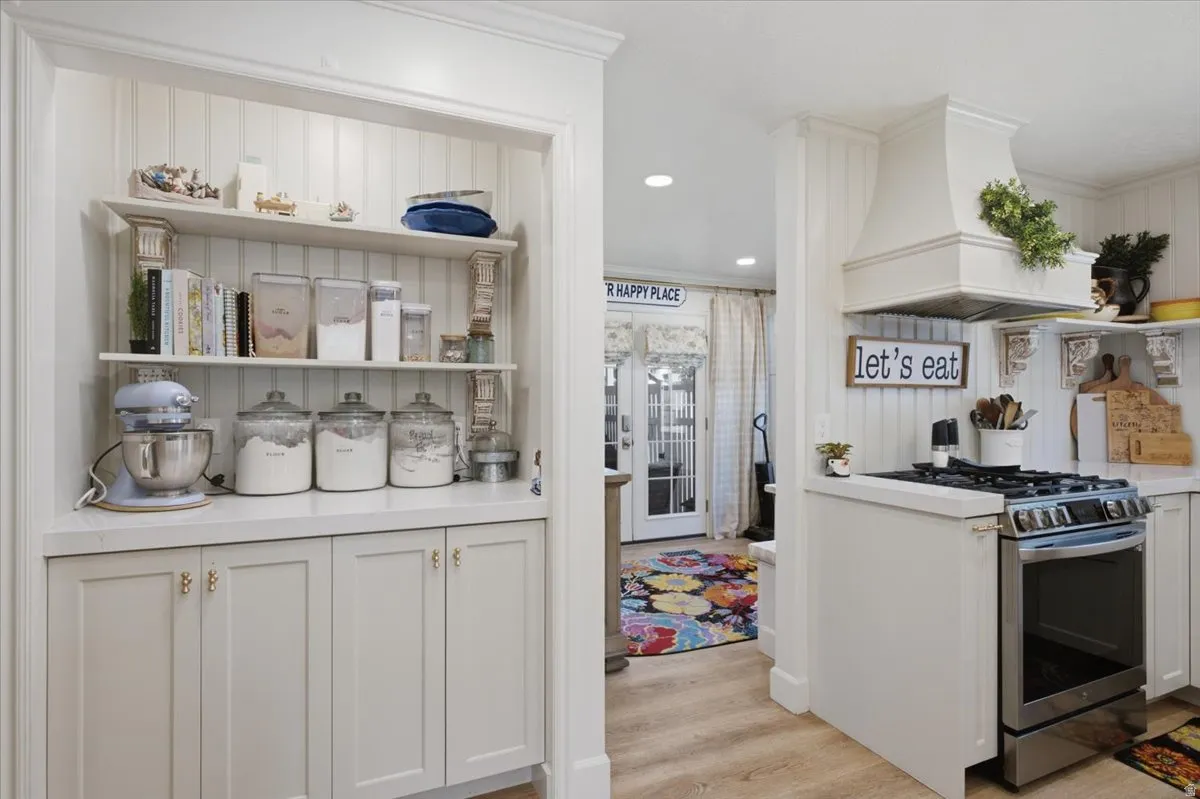 Kitchen featuring beadboard paneling, built-in shelving, white cabinetry with gold hardware, a range hood, and stainless steel stove