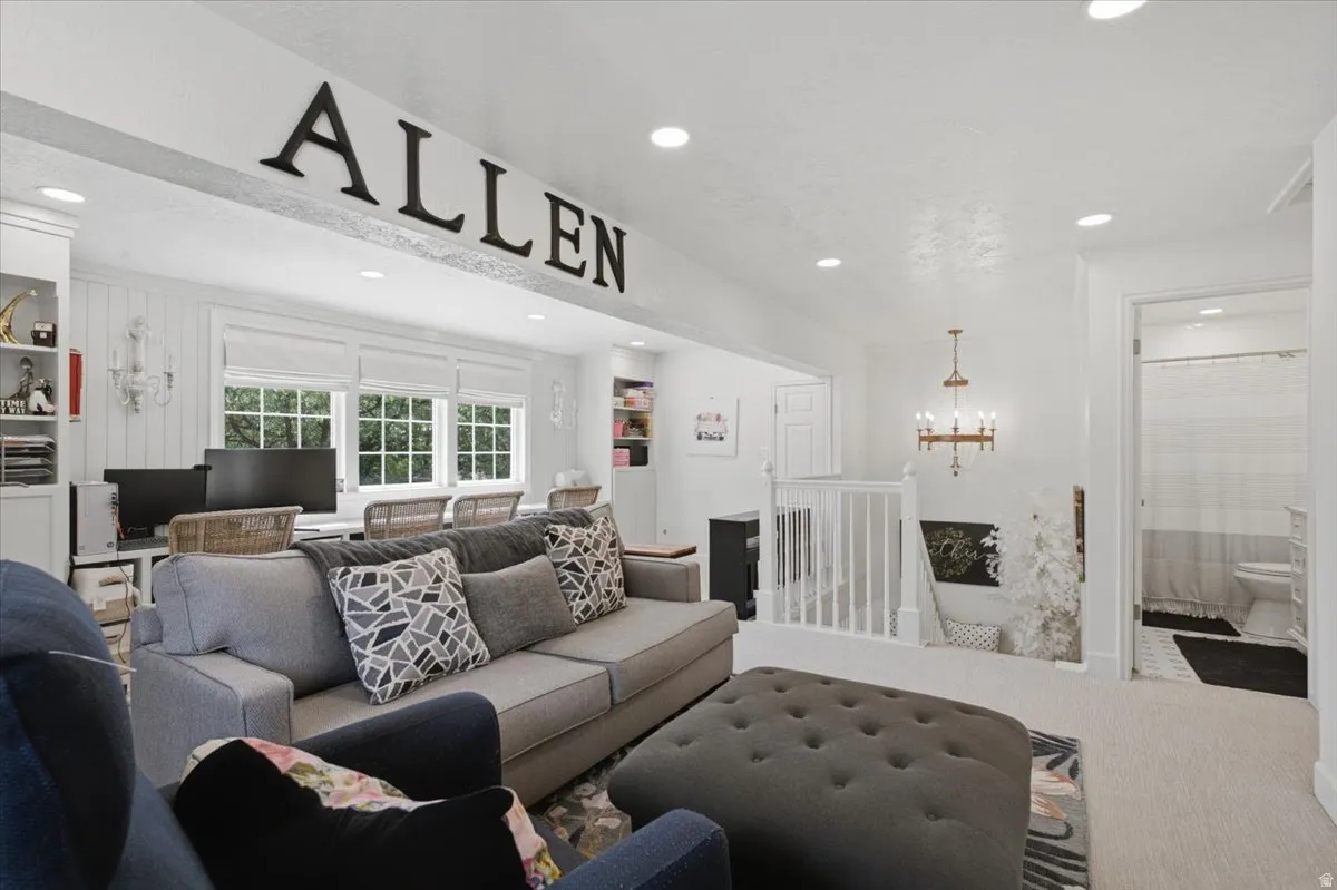Open-concept living space featuring recessed lighting, a built-in desk area with multiple windows, a stairway with white balusters, and a visible bathroom entrance with a glass shower door