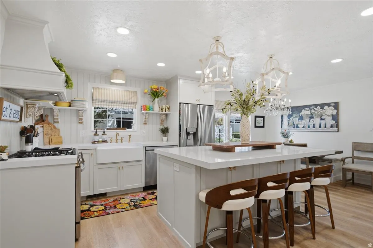 Kitchen featuring an expansive island with seating, pendant lighting, stainless steel appliances, a farmhouse sink, and wood-finish flooring